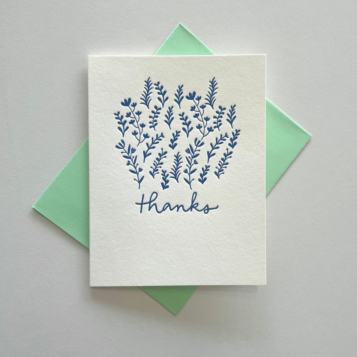 A card with blue floral illustrations and text saying “thanks” with a green envelope against a gray background