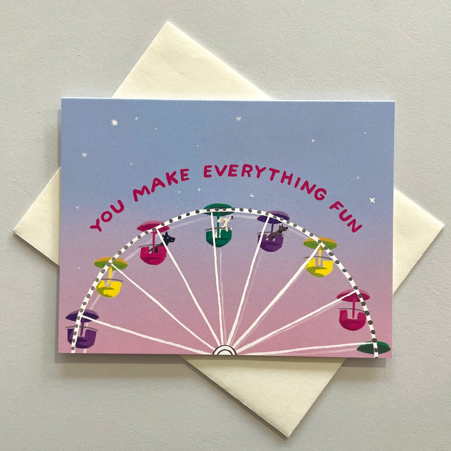A greeting card with a colorful illustration of a Ferris wheel and the text 'You MAKE EVERYTHING FUN' on it, accompanied by a pale blue background and a blank space for a message.