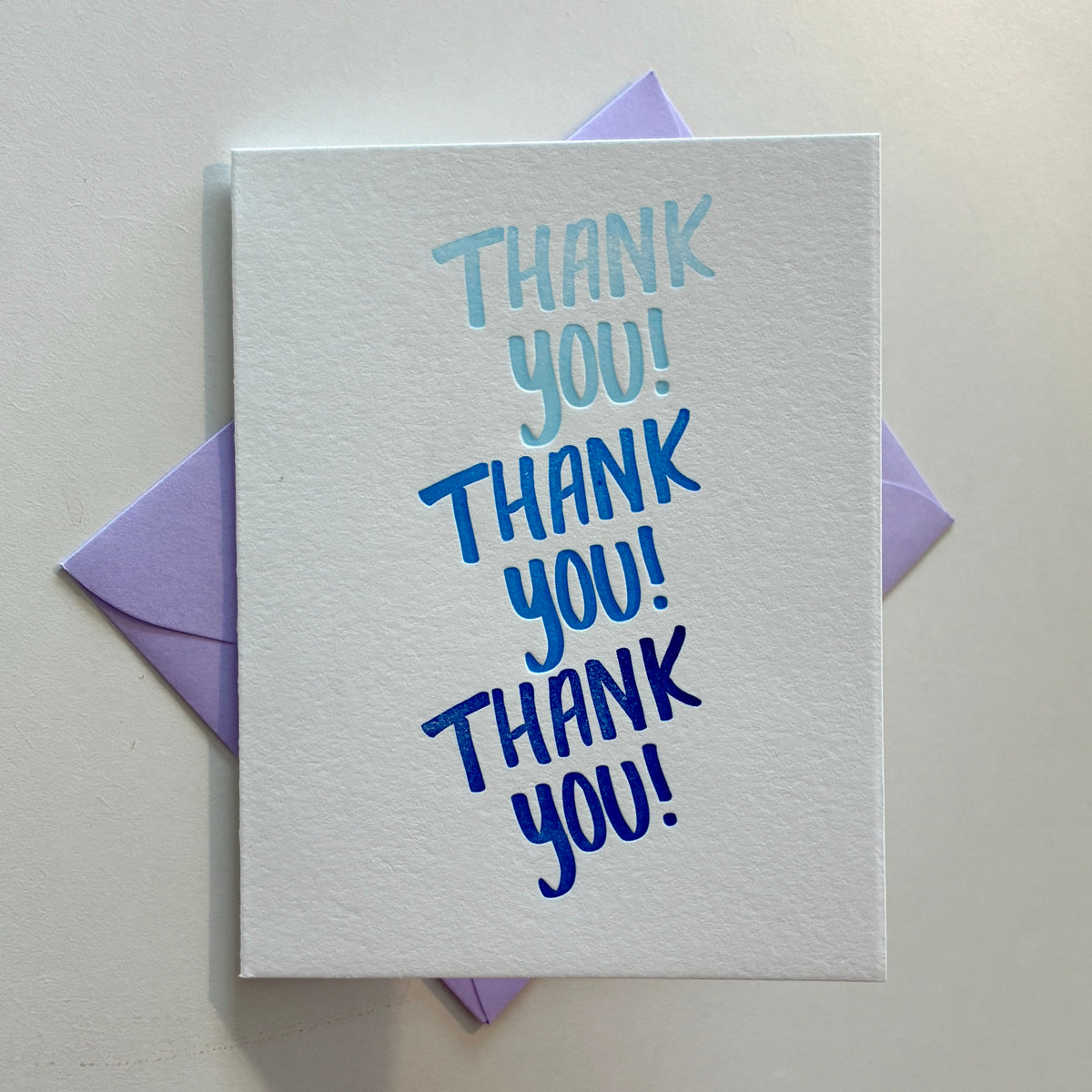 White greeting card with blue text saying “thank you! Thank you! Thank you!”