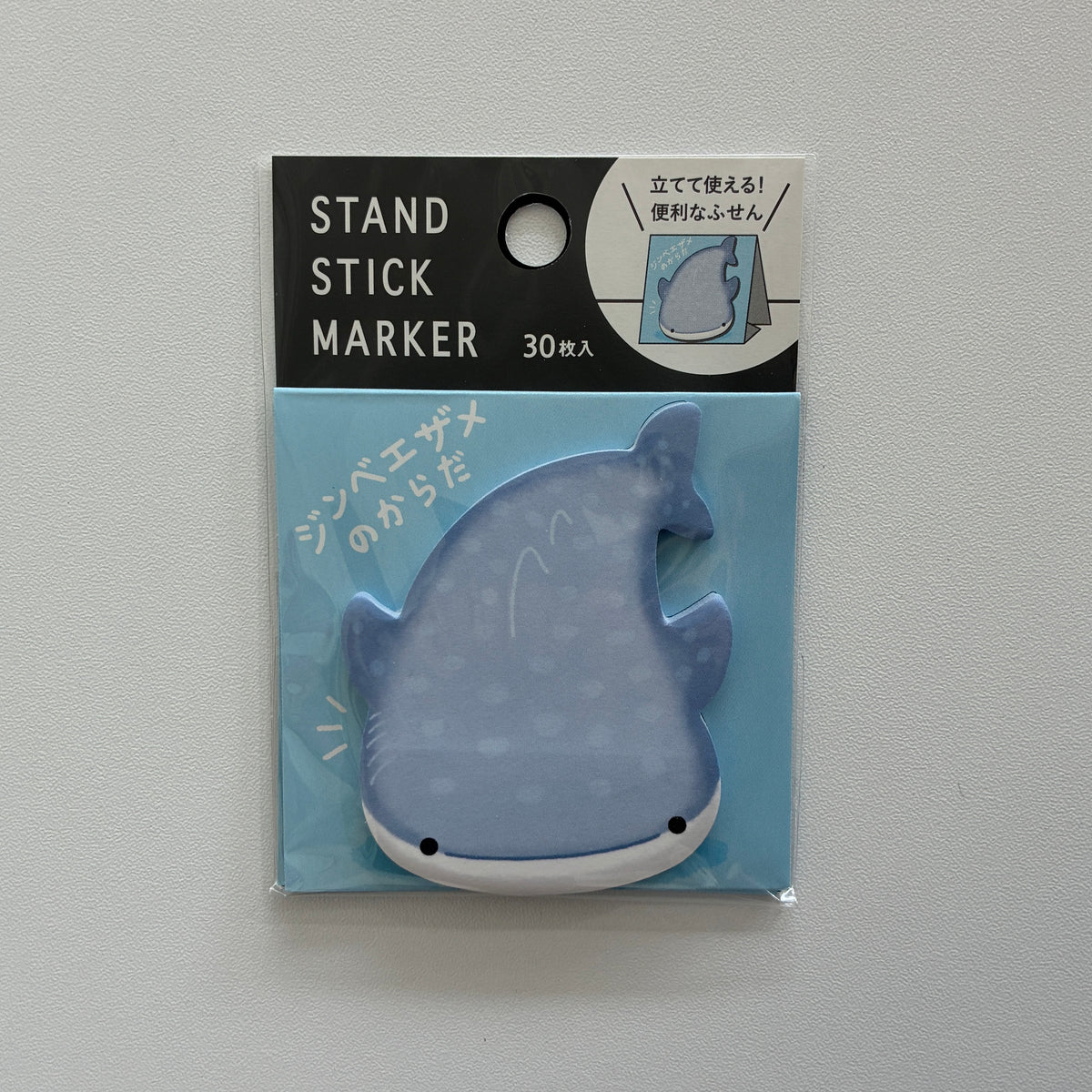 A packaged whale-shaped stand stick marker on a light gray background. The marker is light blue with white spots and a white underside, shown inside a clear blister pack with a black header card that reads 'STAND STICK MARKER' and '30枚入'.