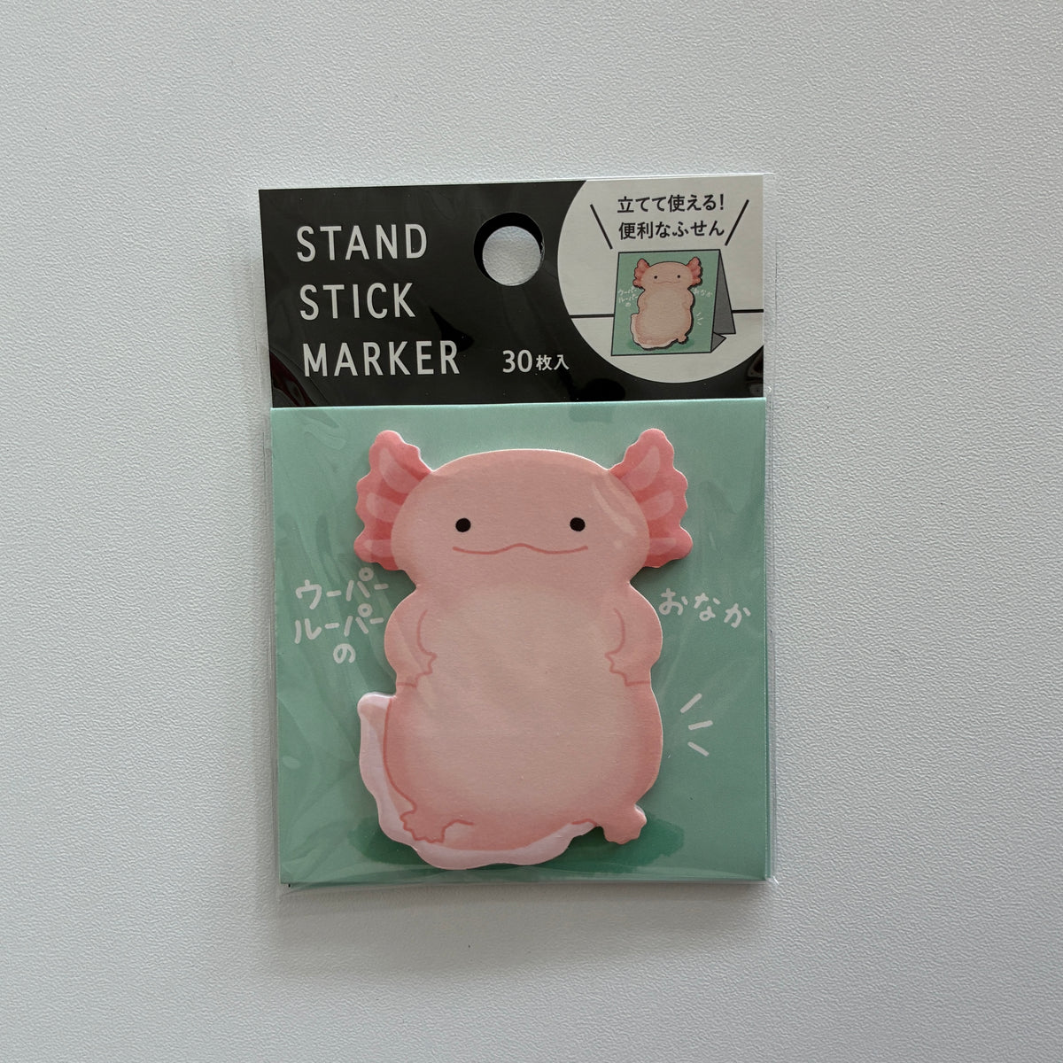 A pink axolotl-shaped stand stick marker in its original packaging, featuring a black and mint green header card with white text.