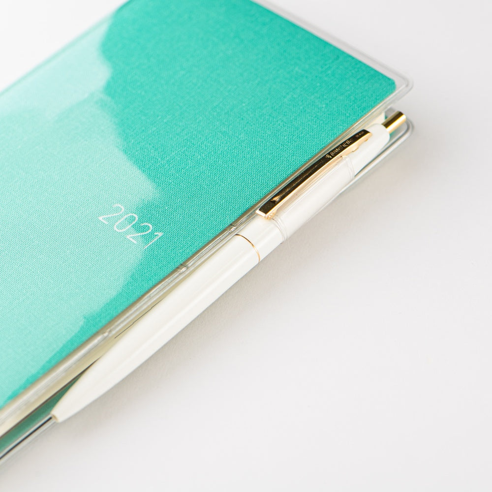 A close-up of a 2021 pocket calendar with a textured mint green cover and a white pen resting inside a clear plastic sleeve, set against a clean white background.