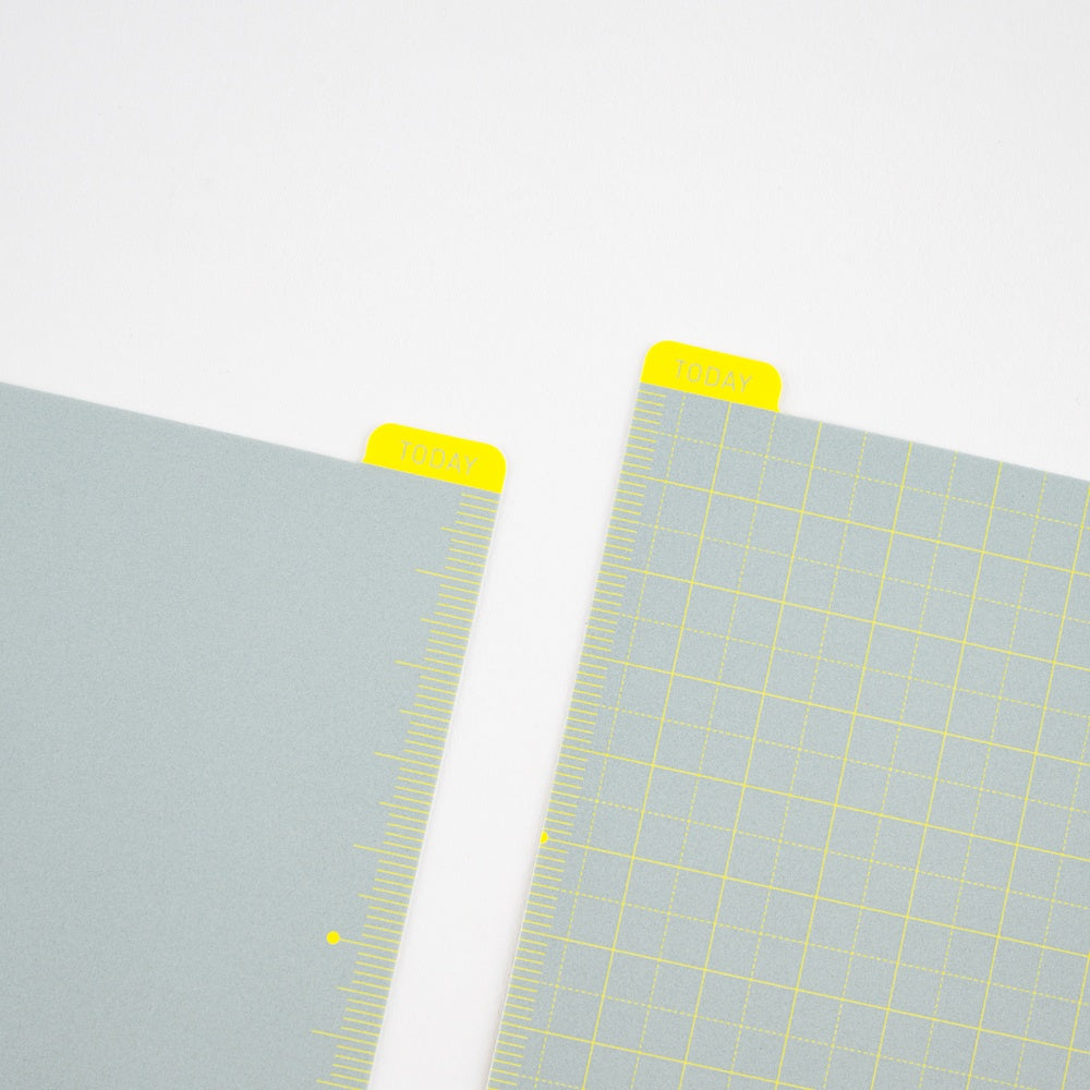 Two pencil boards with grid patterns and yellow corner tabs on a light gray background