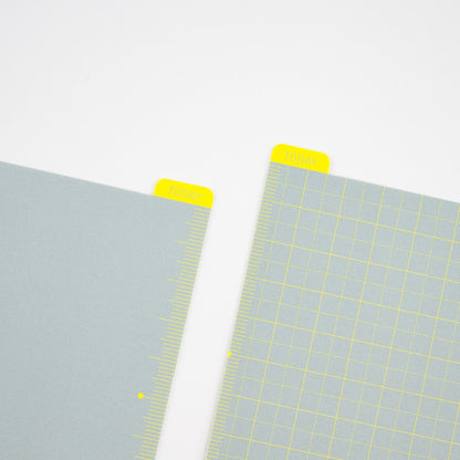Two pencil boards with grid patterns and yellow corner tabs on a light gray background