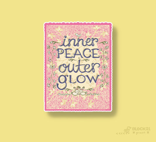A square art print with a pink floral border and the text 'inner PEACE outer GLOW' in dark blue script, centered on a pale yellow background. A small 'BLOCK21' mark appears in the lower right corner.