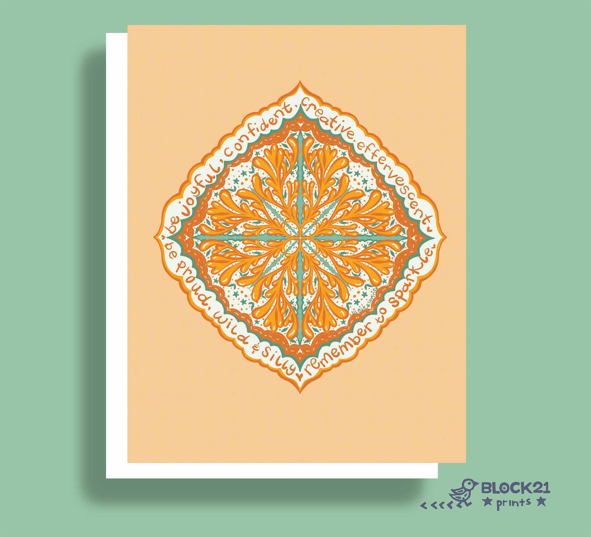 A square art print or greeting card featuring a symmetrical mandala-style floral design in orange, teal, and white on a peach background, shown with a white border and drop shadow against a sage green backdrop. The brand name BLOCK21 prints appears in the bottom right corner.