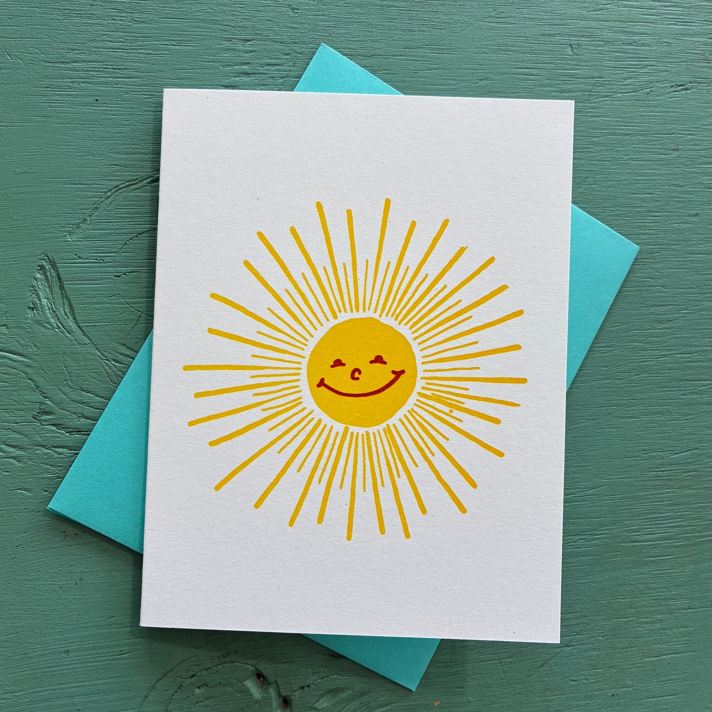 Card with a yellow sun design on a white background, placed on a teal surface.
