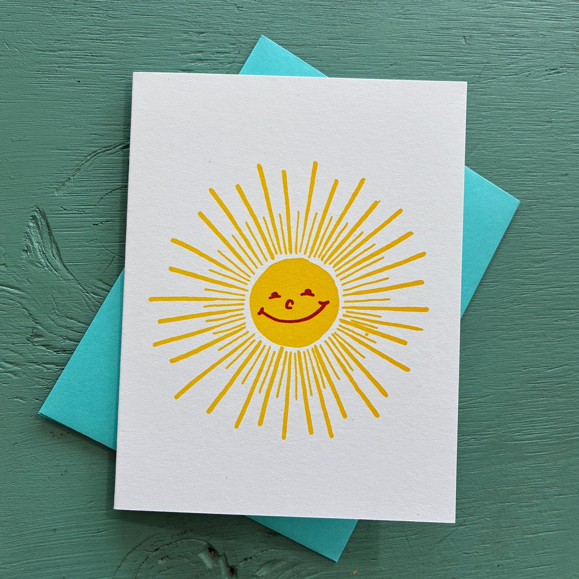 Card with a yellow sun design on a white background, placed on a teal surface.