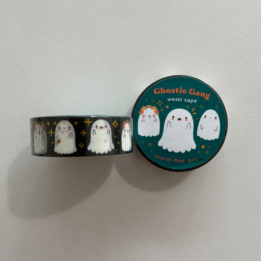 A roll of washi tape and its matching circular lid, featuring cute cartoon ghosts on a dark background. The lid reads 'Ghostie Gang washi tape' and shows three white ghost illustrations on a teal background with small yellow stars.