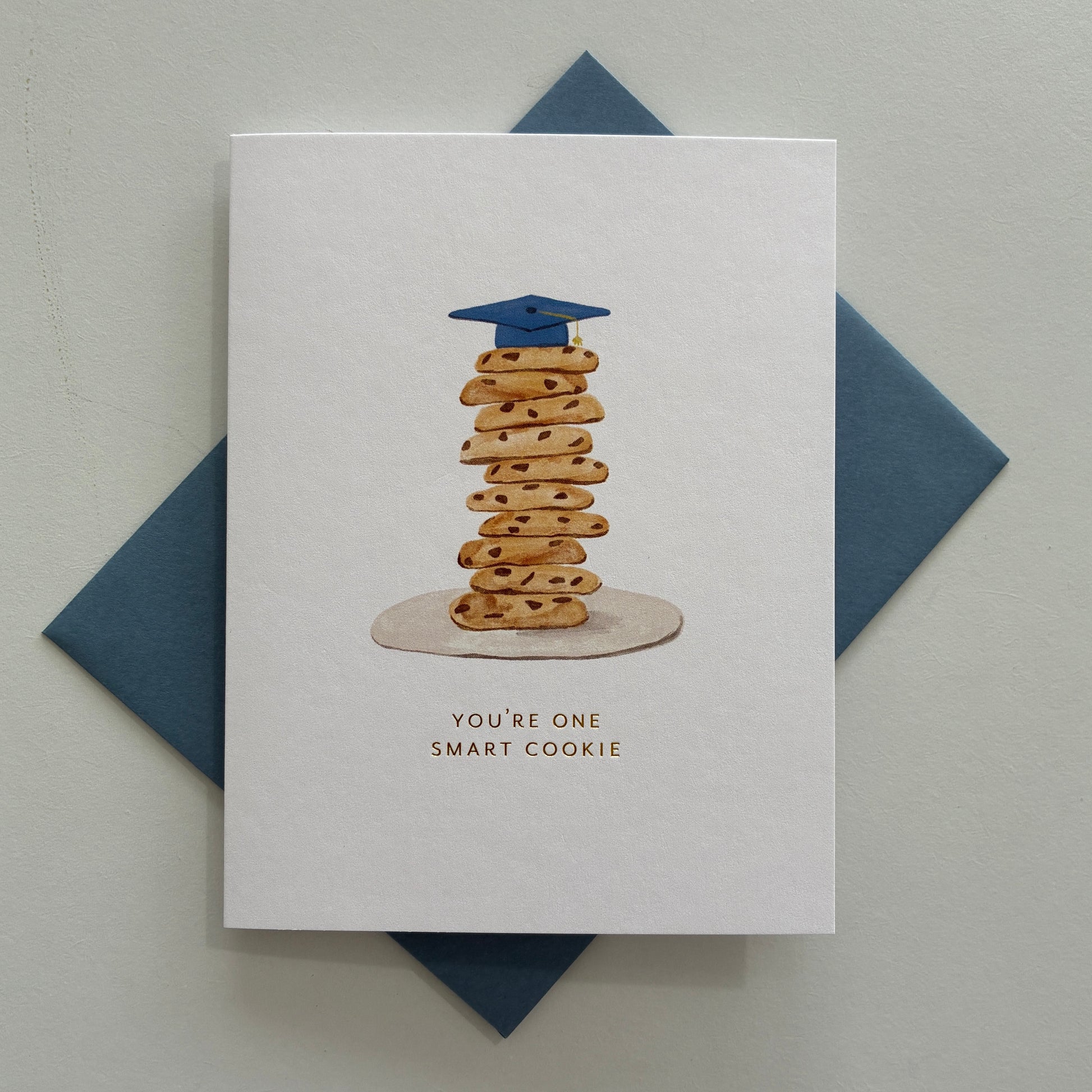 Graduation-themed card with a stack of cookies and a blue cap on a white background with text saying "you're one smart cookie"