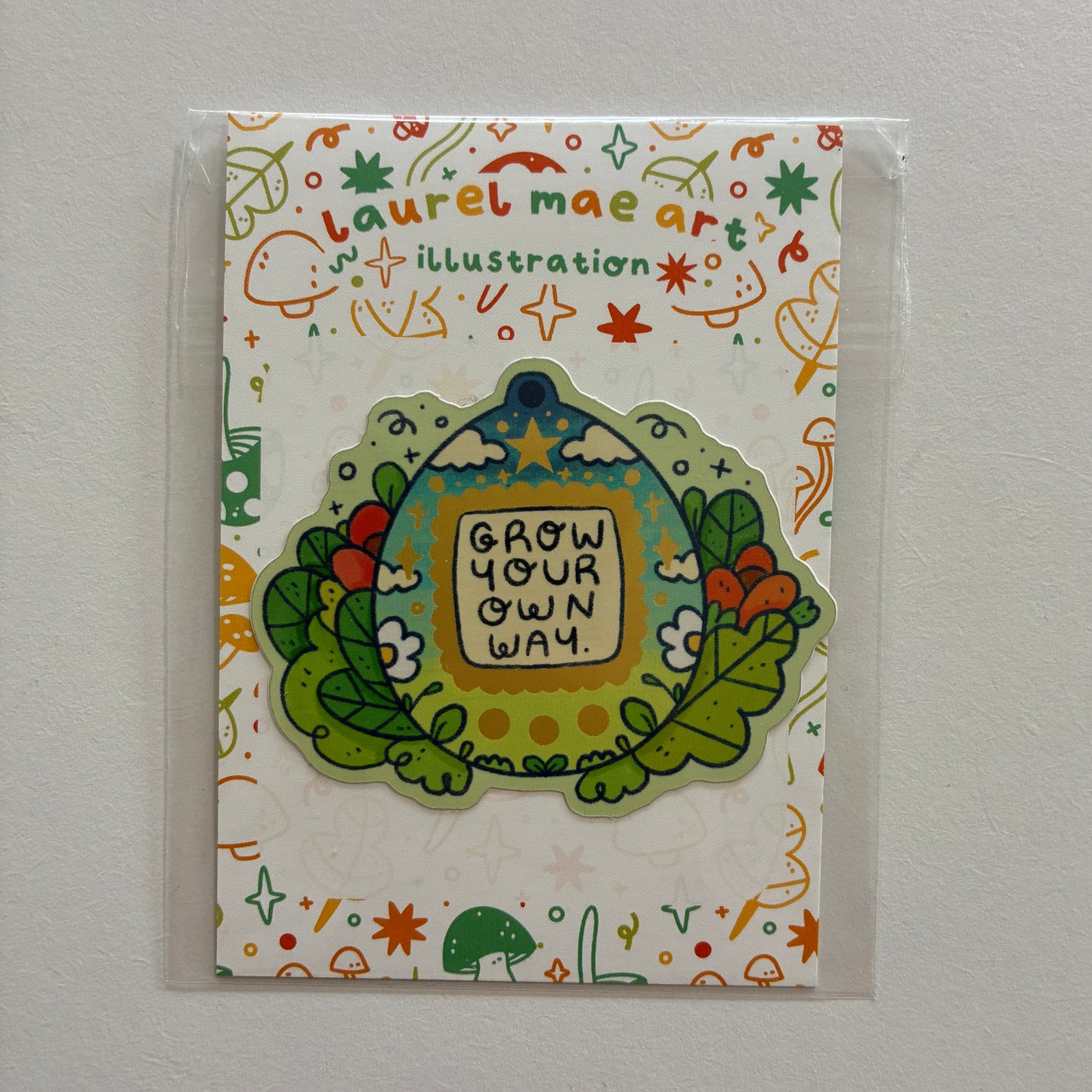 Tamagotchi shaped sticker with text saying “grow your own way”