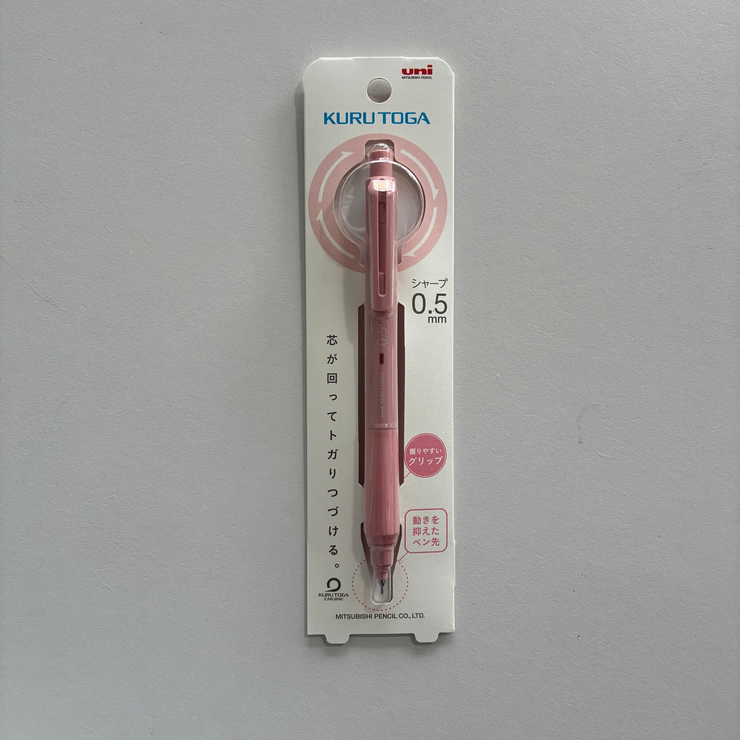 A pink Kuru Toga mechanical pencil in its packaging on a gray background