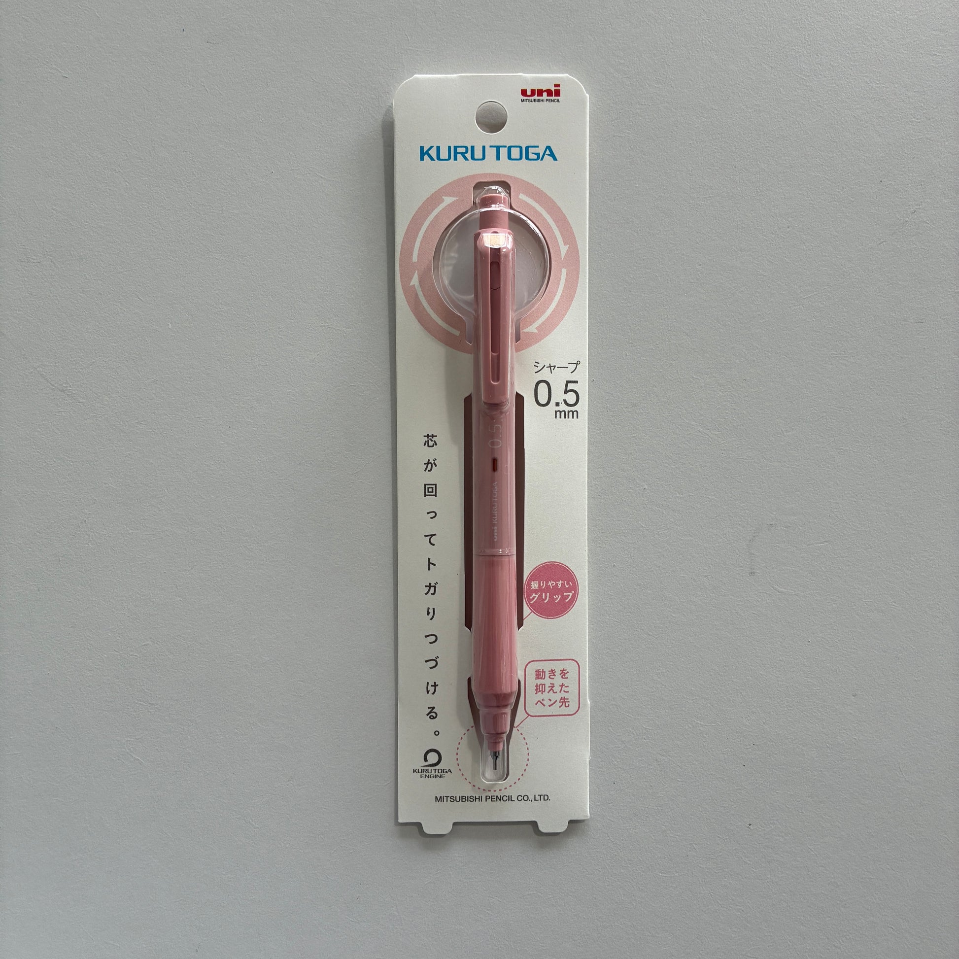 A pink Kuru Toga mechanical pencil in its packaging on a gray background