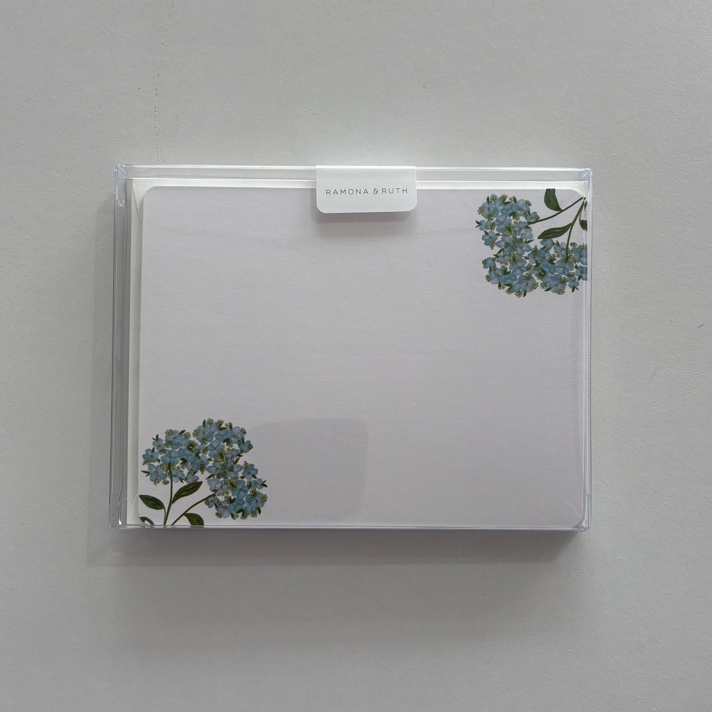 Flat notecard set with floral design in a clear plastic sleeve against a light gray background