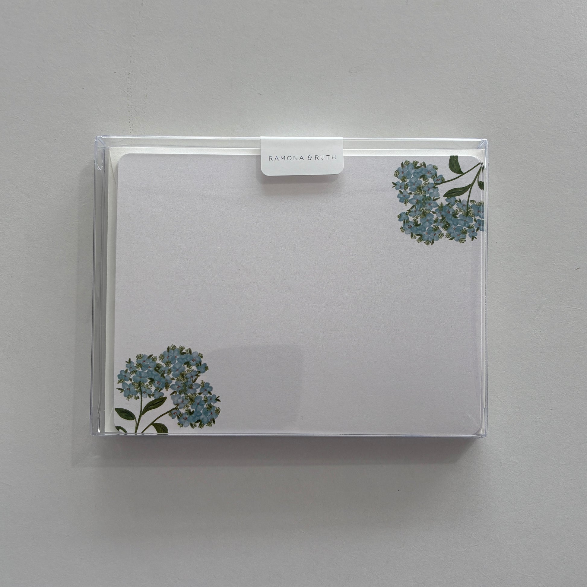 Flat notecard set with floral design in a clear plastic sleeve against a light gray background