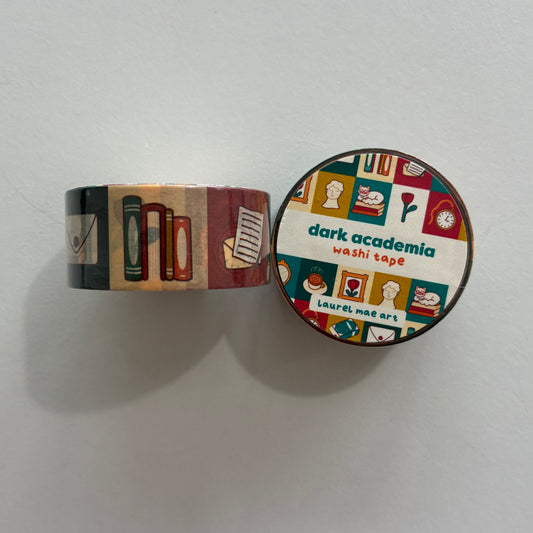 A roll of decorative washi tape with a dark academia theme, shown partially unrolled next to its round lid. The pattern features books, notebooks, coffee cups, and flowers in muted red, green, beige, and brown tones.