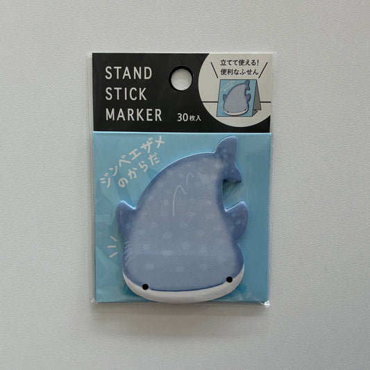 A packaged whale-shaped stand stick marker on a light gray background. The marker is light blue with white spots and a white underside, shown inside a clear blister pack with a black header card that reads 'STAND STICK MARKER' and '30枚入'.