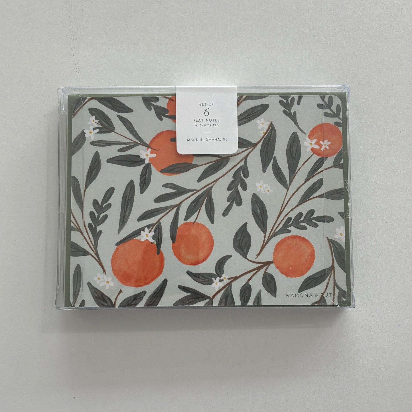 Pack of flat notes with floral design and oranges on a gray background