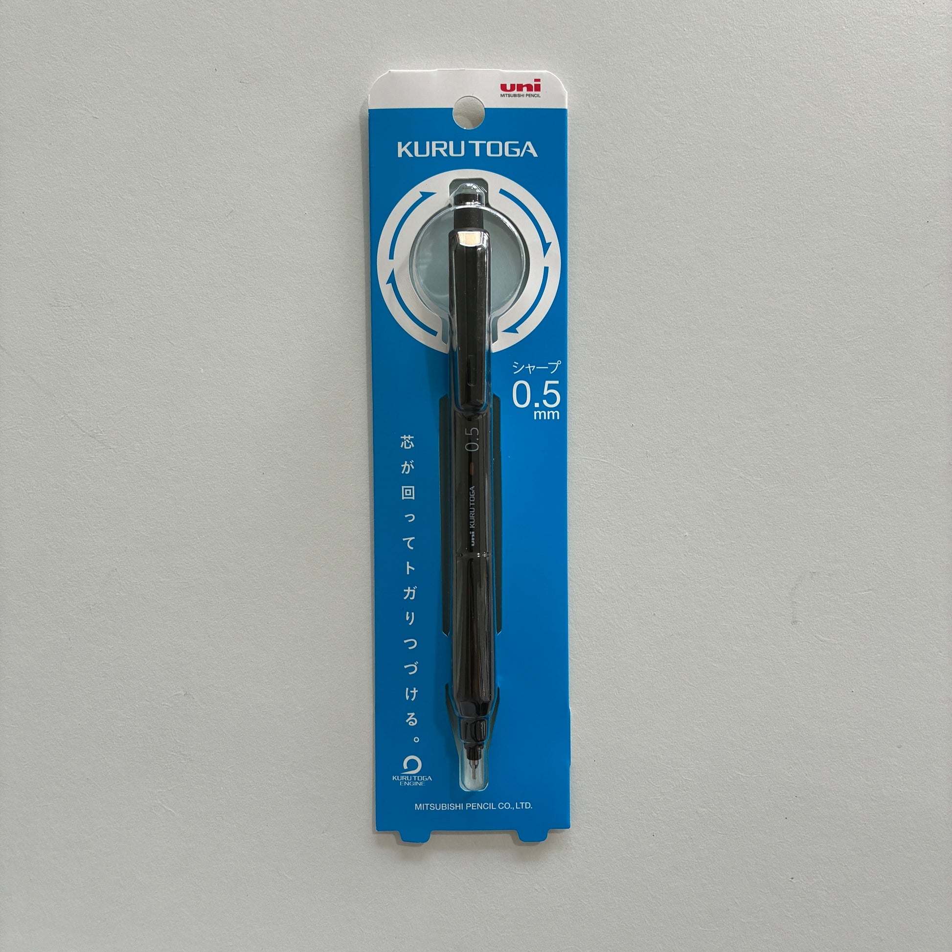 A black Kuru Toga mechanical pencil in its packaging on a gray background