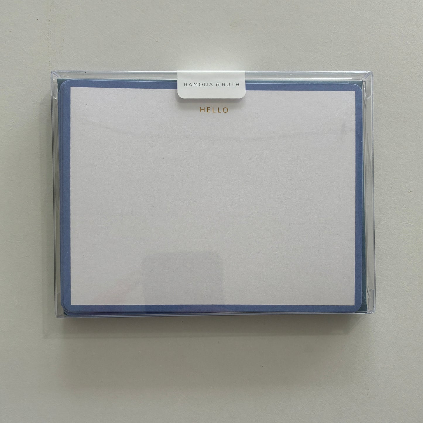 Packaged set of stationery with "HELLO" written in gold foil with a clear cover on a light gray background