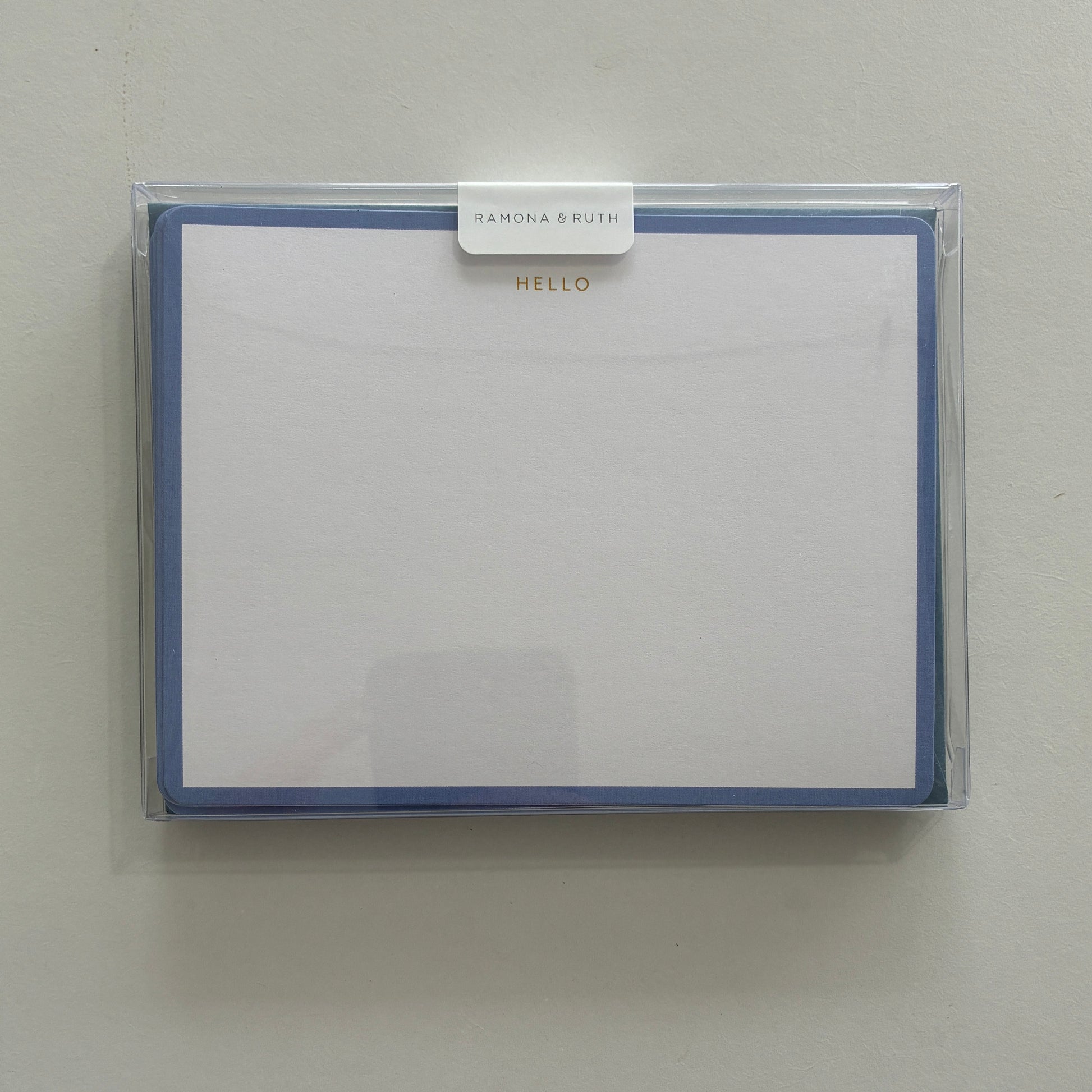 Packaged set of stationery with "HELLO" written in gold foil with a clear cover on a light gray background