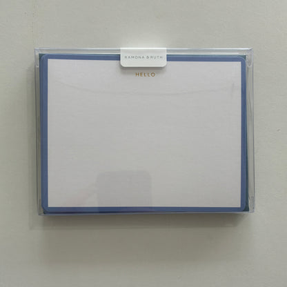 Packaged set of stationery with "HELLO" written in gold foil with a clear cover on a light gray background