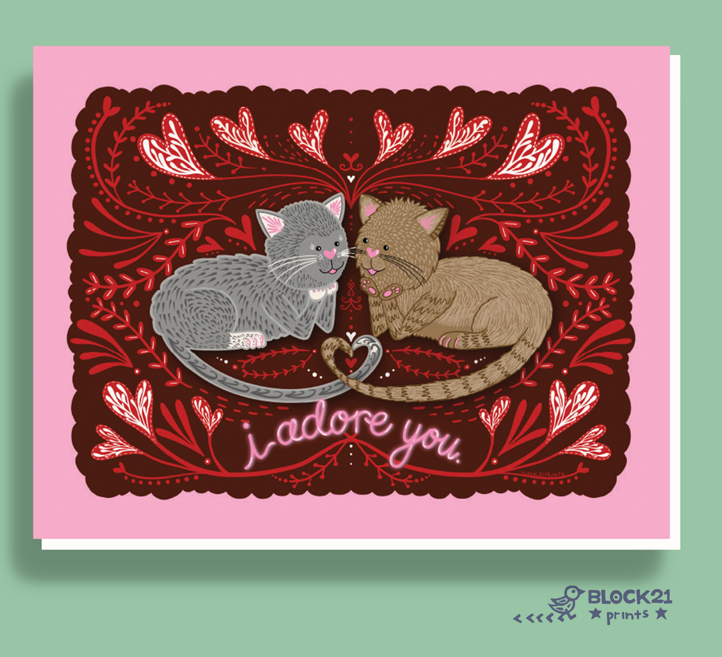 A square greeting card featuring an illustration of two cats facing each other under ornate red floral motifs, with the text 'I adore you.' on the card.