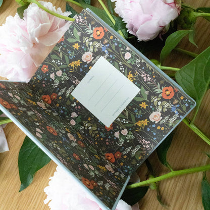 Floral-patterned notebook surrounded by pink flowers and green leaves.