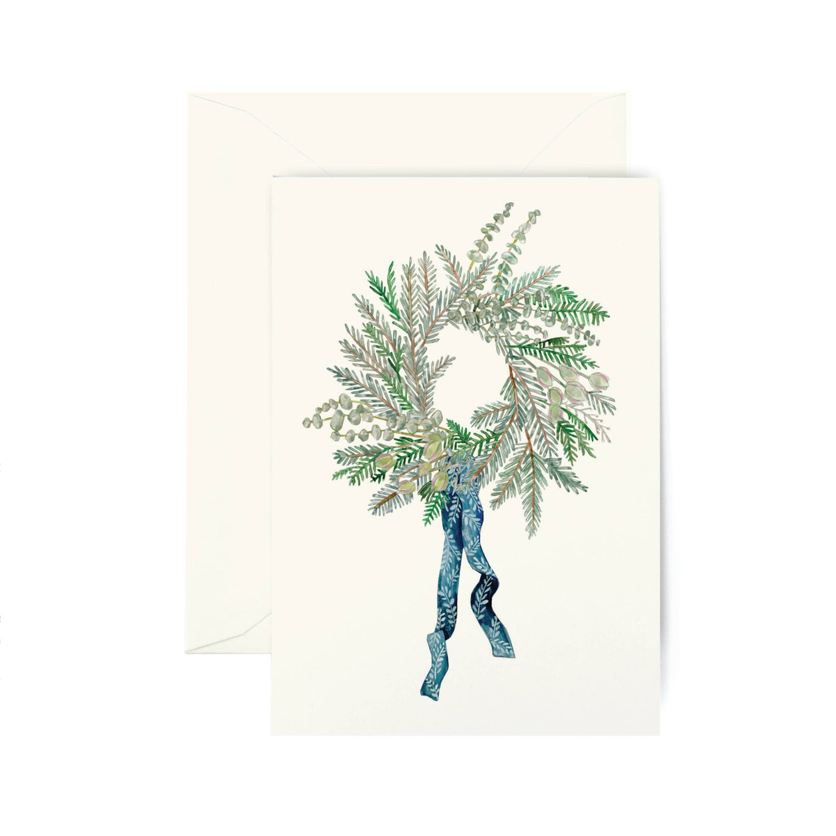 A cream-colored greeting card featuring an illustration of a winter wreath with green and silver pine branches tied with a blue ribbon, shown with a matching cream envelope behind it on a white background.